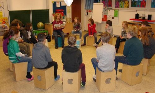 Sitzkreis Kinder in der Erwin Roeske Grundschule. Die Lehrerin liest etwas vor